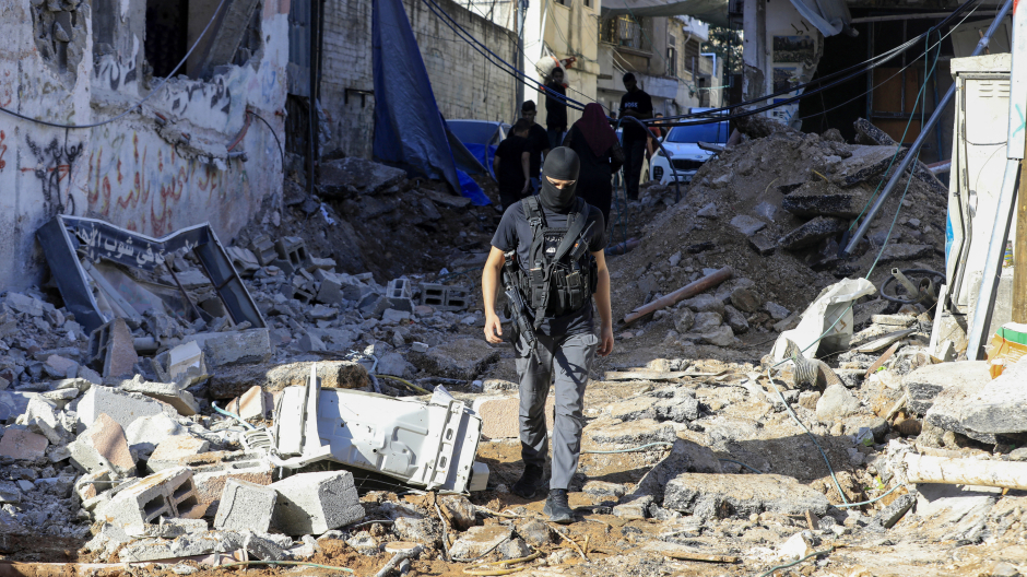 Un palestino armado camina entre los escombros de un edificio dañado durante una redada de tropas israelíes en el campo de refugiados de Nur Shams