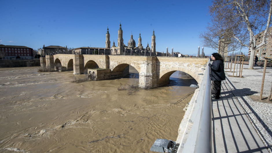 Dos personas observan la crecida del río Ebro a su paso por Zaragoza