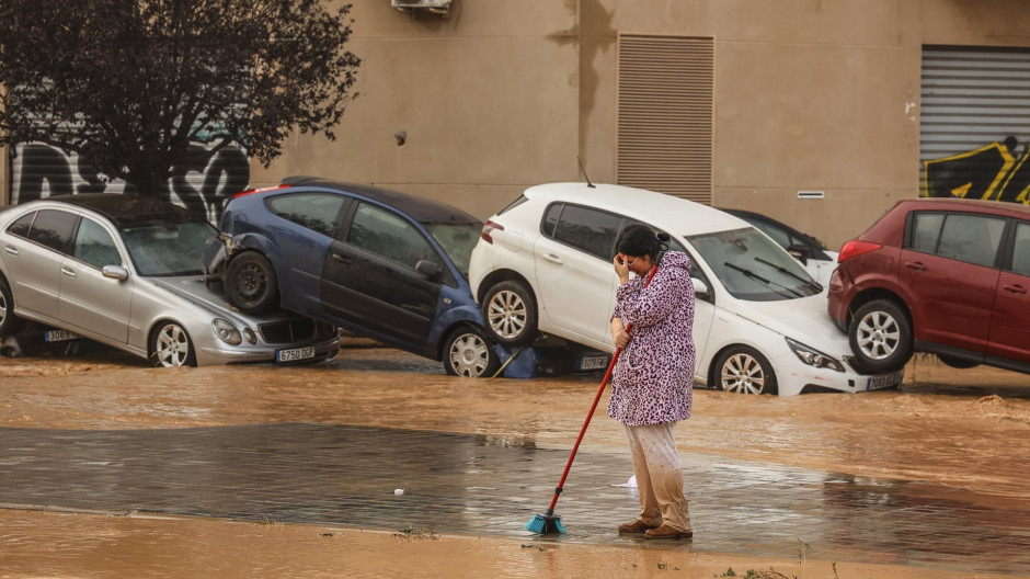 Una mujer realiza labores de limpieza junto a vehículos destrozados tras el paso de la DANA por el barrio de La Torre de Valencia