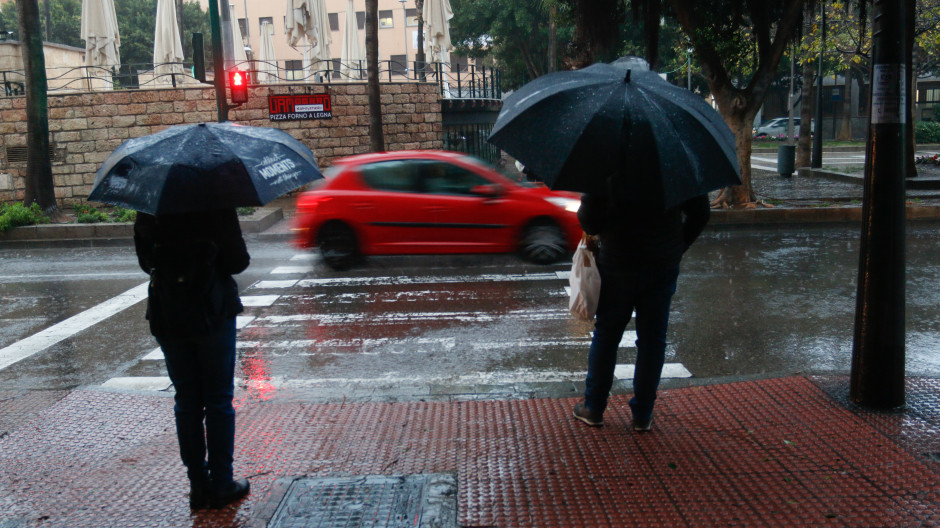 Unos viandantes caminan con fuertes rachas de viento y lluvia en una calle de Almería
