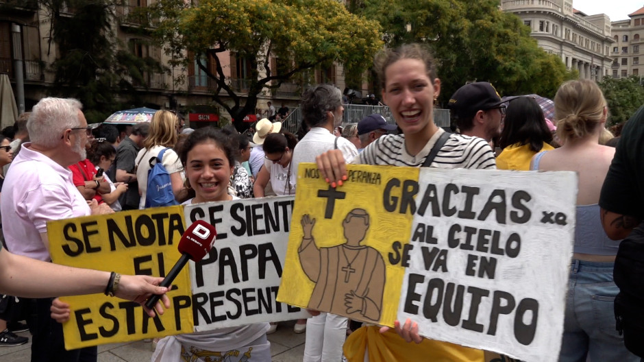 Dos jóvenes sostienen carteles con mensajes para el Santo Padre León XIV frente a la catedral de Barcelona