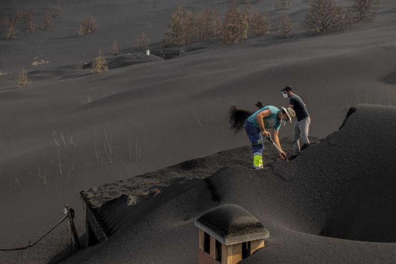 Personas limpiando el tejado de las casas cubierto por la ceniza del volcán de La Palma en Las Manchas