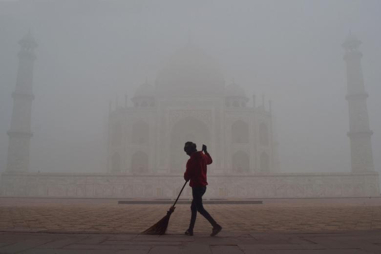 Un hombre barre frente al Taj Mahal en medio de una densa niebla en una fría mañana de invierno en Agra