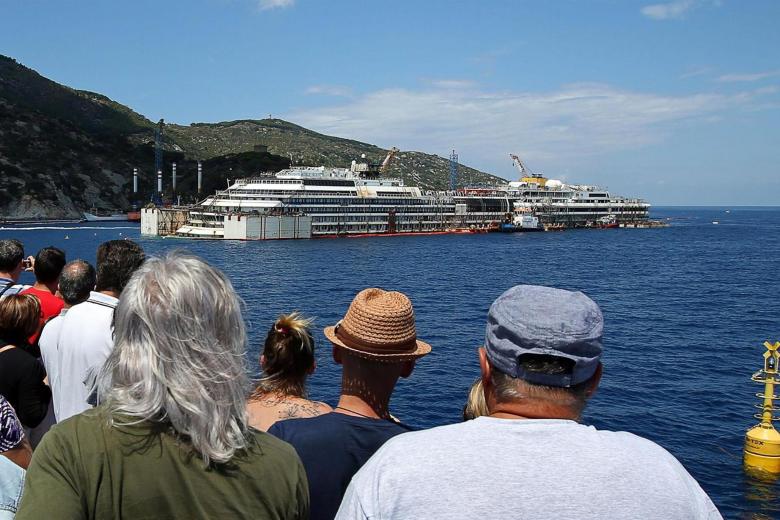 Varios turistas observan los trabajos de recuperación del Costa Concordia