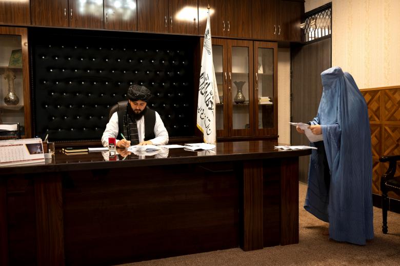 Esta foto tomada el 17 de enero de 2022 muestra a una mujer vestida con burka que espera recibir la firma de su prueba de residencia en la oficina del alcalde de Maymana, Damullah Mohibullah Mowaffaq (izquierda), en Maymana, capital de la provincia afgana de Faryab, al noroeste del país. El nuevo alcalde de Maymana tiene un rostro aniñado, un encanto fácil y una aparente fuente de buena voluntad por parte de los electores de la capital provincial afgana. Pero Damullah Mohibullah Mowaffaq tiene fama de ser uno de los mejores francotiradores en las filas de los talibanes, que hasta el verano pasado hicieron la guerra para tomar el control del país
