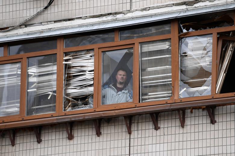 A man looks out from a balcony of a damaged residential building at Koshytsa Street, a suburb of the Ukrainian capital Kyiv, where a military shell allegedly hit, on February 25, 2022. - Russian forces reached the outskirts of Kyiv on Friday as Ukrainian President Volodymyr Zelensky said the invading troops were targeting civilians and explosions could be heard in the besieged capital. Pre-dawn blasts in Kyiv set off a second day of violence after Russian President Vladimir Putin defied Western warnings to unleash a full-scale ground invasion and air assault on Thursday that quickly claimed dozens of lives and displaced at least 100,000 people. (Photo by Daniel LEAL / AFP)