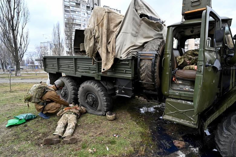 Un médico militar ucraniano examina el cuerpo de un militar ruso que vestía un uniforme de servicio ucraniano que yace al lado de un vehículo después de que él y los miembros de un grupo de asalto recibieron disparos durante una escaramuza en la capital ucraniana de Kiev.