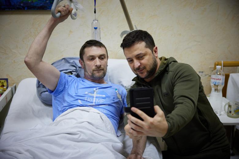 In this handout picture released and taken by Ukrainian Presidency Press Office on March 13, 2022, Ukrainian President Volodymyr Zelensky (L) snaps a selfie with an injured man laying on a bed during a visit at a military hospital following fightings in the Kyiv region. - According to the presidency official website, Zelensky made a visit to the hospital to "award militaries with orders and medals for courage and dedication, and to honor the hospital staff for exemplary work in difficult conditions". (Photo by Handout / UKRAINIAN PRESIDENTIAL PRESS SERVICE / AFP) / RESTRICTED TO EDITORIAL USE - MANDATORY CREDIT "AFP PHOTO / UKRAINIAN PRESIDENTIAL PRESS SERVICE " - NO MARKETING - NO ADVERTISING CAMPAIGNS - DISTRIBUTED AS A SERVICE TO CLIENTS - RESTRICTED TO EDITORIAL USE - MANDATORY CREDIT "AFP PHOTO / Ukrainian presidential press service " - NO MARKETING - NO ADVERTISING CAMPAIGNS - DISTRIBUTED AS A SERVICE TO CLIENTS /