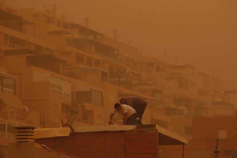 Unas personas trabajan en Aguadulce, Roquetas de Mar ( Almería) que ha amanecido este martes bajo los efectos de la intensa calima que ha cubierto de polvo sahariano buena parte de España