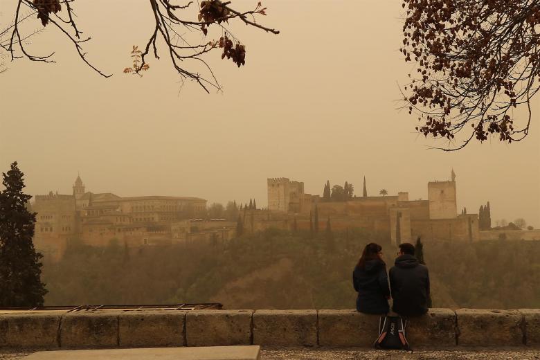 Dos personas observan la Alhambra de Granada desde el Mirador de San Nicolás con el cielo cubierto con la intensa calima debido al polvo procedente del desierto del Sáhara