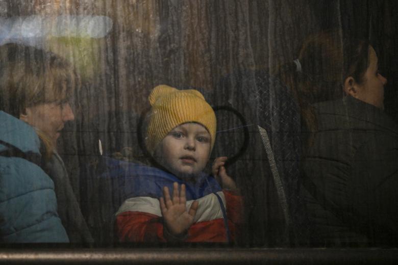 A child greets from the window of a bus after crossing the Ukrainian border with Poland at the Medyka border crossing, southeastern Poland, on March 14, 2022. - Over 2.8 million refugees have fled Ukraine since the invasion began, more than half going to Poland, according to the UN refugee agency. (Photo by Louisa GOULIAMAKI / AFP)