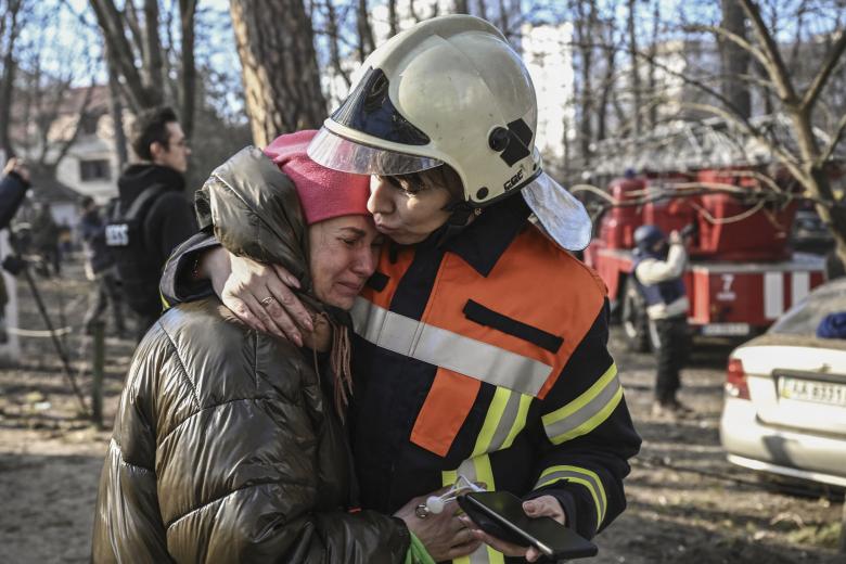 An evacuated resident is comforted by a rescue staff outside a burning apartment building in Kyiv on March 15, 2022, after strikes on residential areas killed at least two people, Ukraine emergency services said as Russian troops intensified their attacks on the Ukrainian capital. - A series of powerful explosions rocked residential districts of Kyiv early today killing two people, just hours before talks between Ukraine and Russia were set to resume. (Photo by Aris Messinis / AFP)