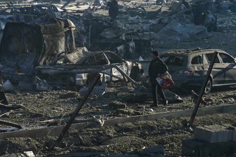 Un hombre pasea a su perro junto a vehículos quemados y escombros luego de un ataque con misiles en el centro comercial Retroville en Kiev