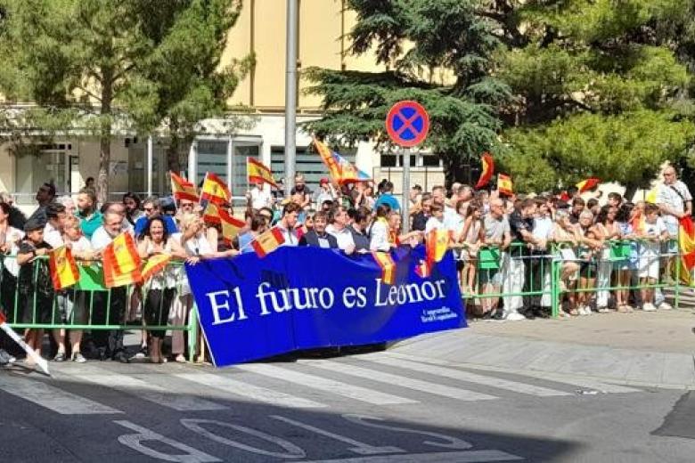 Un grupo de personas recibe a la Princesa con aplausos y banderas de España
