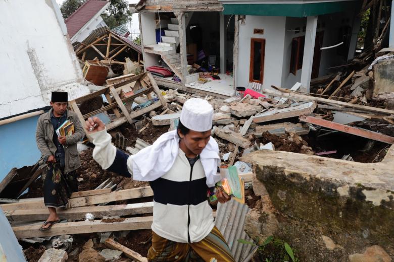 Un estudiante y un maestro pasan junto a su internado islámico derrumbado a causa de un terremoto de magnitud 5,6