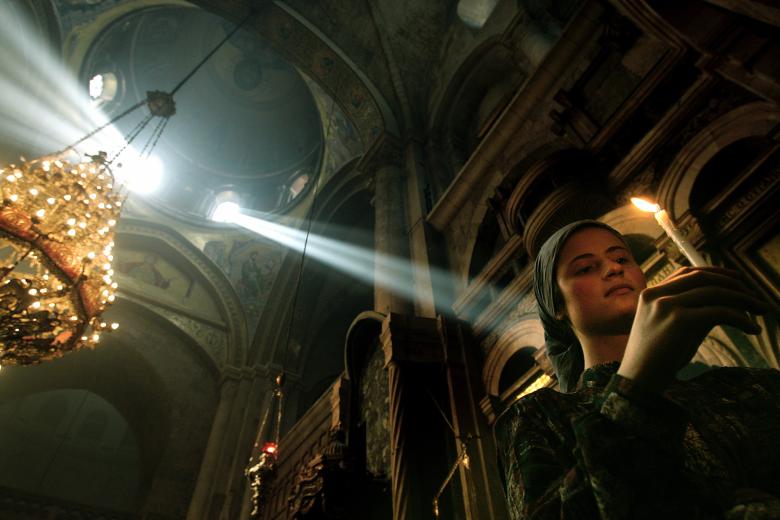 As a Christian Orthodox worshipper holds a burning candle, rays of sunlight shine through windows in the dome of the Church of the Holy Sepulcher, traditionally believed to be the burial place of Jesus Christ, during the ceremony of the Holy Fire, part of the Christian Orthodox Easter celebrations in Jerusalem's Old City Saturday April 30, 2005. .(AP Photo/Emilio Morenatti)