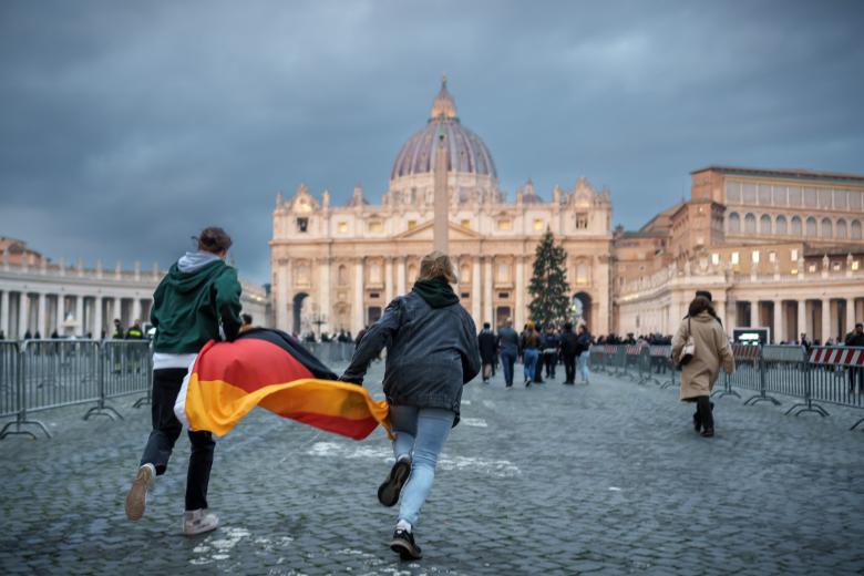 Two young people with a Germany flag walk in the morning across St. Peter's Square in front of St. Peter's Basilica, where the body of the late Pope Emeritus Benedict XVI is laid out. The Pope Emeritus had died at the age of 95. (To dpa "Deceased Pope Benedict XVI is laid out in St. Peter's Basilica.") 
bavaria church Pope religion Religion and Belief ReligiÃ³n Rome Vatican Germany