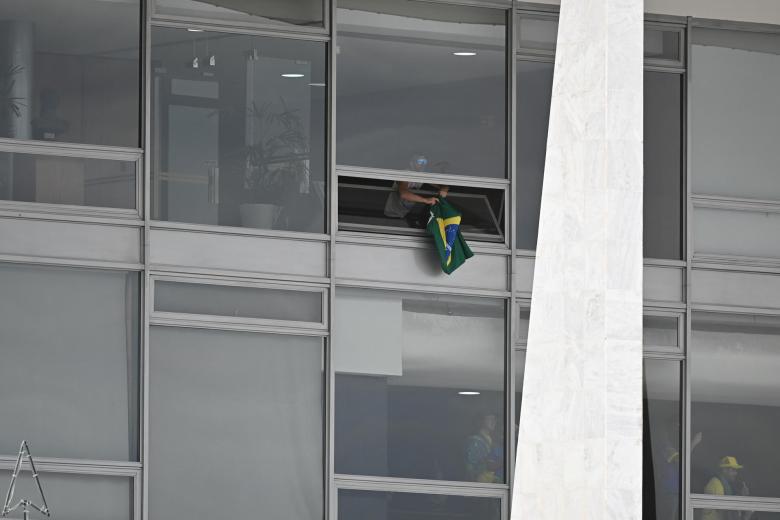 Un manifestante cuelga una bandera brasileña desde el interior del Congreso invadido