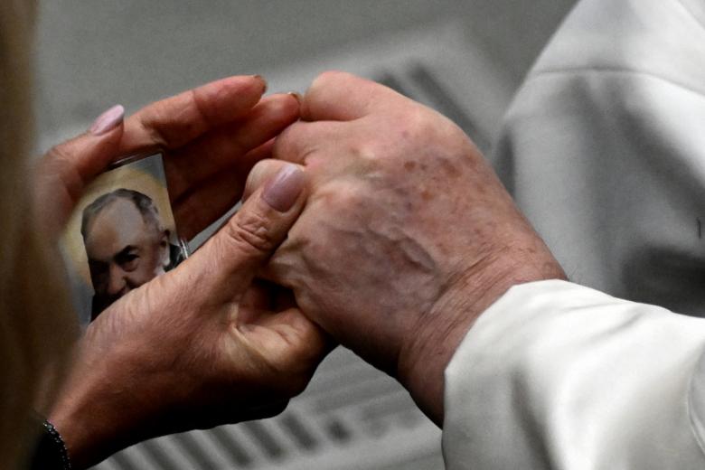 Pope Francis (R) holds an attendee's hand during the weekly general audience on January 25, 2023 at Paul-VI hall in The Vatican. (Photo by Tiziana FABI / AFP)