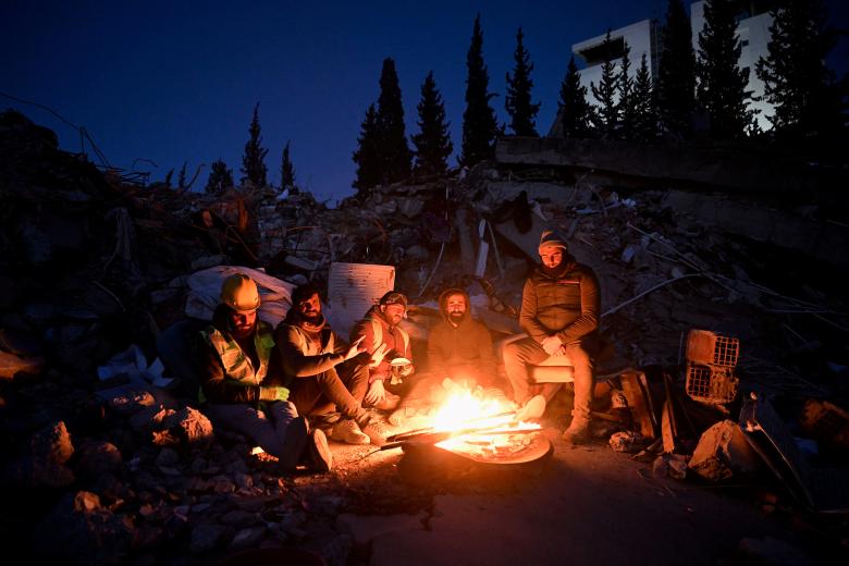 Relatives of victims warm with a fire next to rubble of collapsed buildings, as rescue teams continue to search victims and survivors, after a 7.8 magnitude earthquake struck the border region of Turkey and Syria earlier in the week, in Kahramanmaras on February 13, 2023. - The death toll from a catastrophic earthquake that hit Turkey and Syria climbed above 35,000 on February 13, 2023, with search and rescue teams starting to wind down their work. (Photo by OZAN KOSE / AFP)