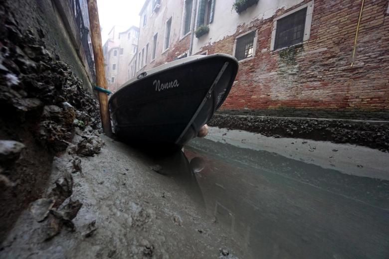 Un pequeño bote yace en el fondo de un canal durante la marea baja. Venecia ha luchado durante muchos días contra este problema.