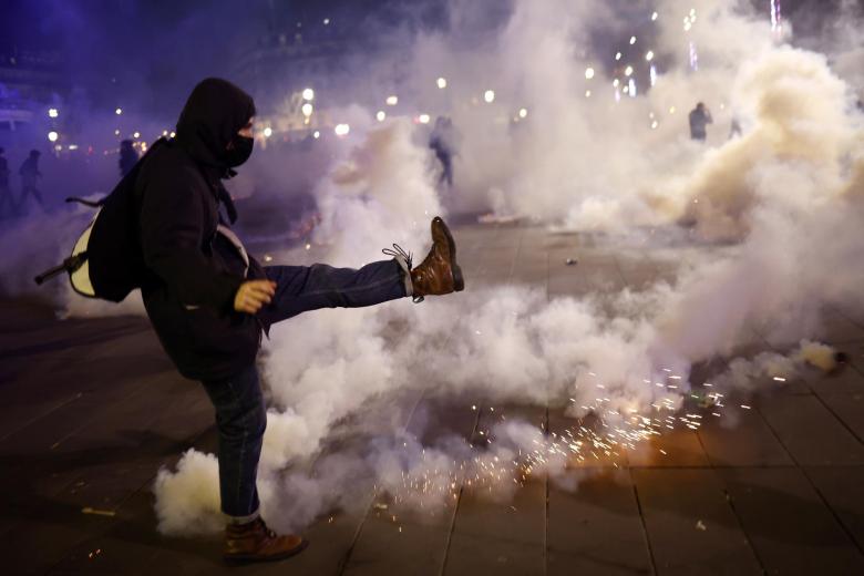Un manifestante enmascarado lanza un bote de gas lacrimógeno a las fuerzas policiales en la plaza Republique, durante una manifestación contra la reforma de las pensiones del gobierno en París.