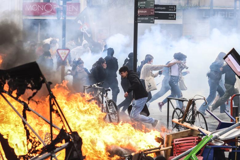 Manifestantes corren entre el humo de gases lacrimógenos junto a una hoguera callejera al margen de una manifestación en el marco de una jornada nacional de huelgas y protestas, una semana después de que el Gobierno francés sacara adelante en el Parlamento una reforma de las pensiones sin someterla a votación, amparándose en el artículo 49.3 de la Constitución, en Toulouse, sur de Francia.