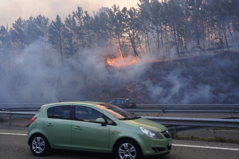 GRAF667. LUARCA, 31/03/2023.- Un coche circula por la A8 en Luarca, ante las llamas del incendio registrado en la región asturiana. Asturias registra a primera hora de este viernes 116 incendios forestales, veintiséis más que anoche, una situación que ayer obligó a desalojar a 174 personas de 39 viviendas en la zona occidental y a cortar la autovía A-8 con Galicia. EFE/Paco Paredes