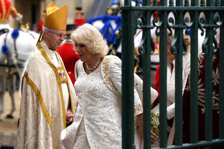 El vestido con abrigo y capa de Camilla es obra de Bruce Oldfield, con bordados dorados muy sofisticados y escote en pico. Oldfield fue en ocasiones proveedor de la princesa Diana. Sus pendientes y collar de chatones, impresionantes en calidad y tamaño.