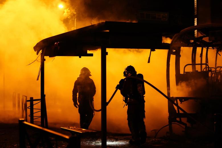 Los bomberos extinguen un autobús quemado durante los enfrentamientos entre los manifestantes y la policía antidisturbios