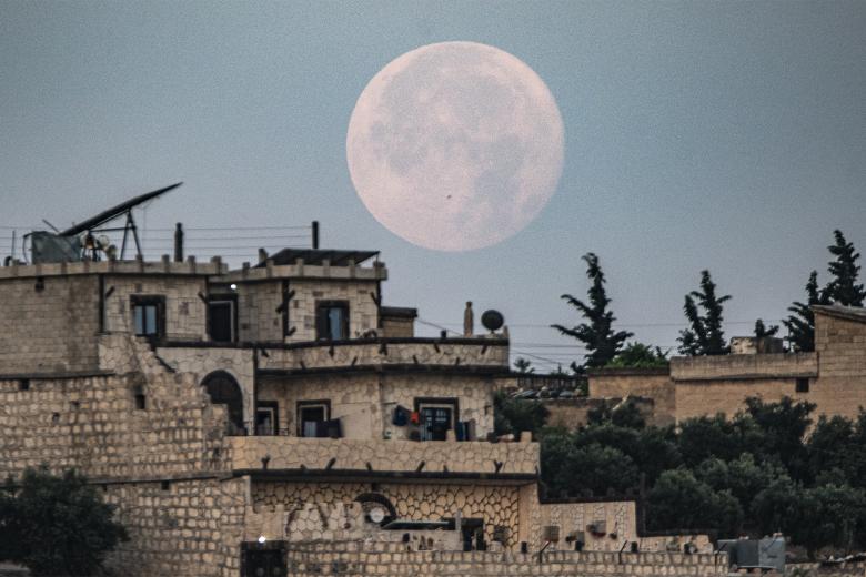 La luna del ciervo se pone detrás de los edificios en la aldea de Deir Ballut en la región de Afrin controlada por los rebeldes de la provincia de Alepo, en el norte de Siria, a principios del 4 de julio de 2023. (Foto de Rami al SAYED / AFP)