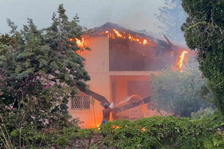 Un hombre rocía agua con un balde mientras arde una casa en el distrito de Tono de Messina, Sicilia