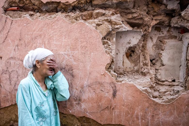Una mujer se lamenta por lo ocurrido frente a un muro medio derruido.