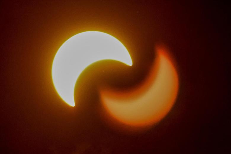 El eclipse solar anular parcial y su reflejo son visibles a través de las nubes en College Park, Georgia, EE. UU.