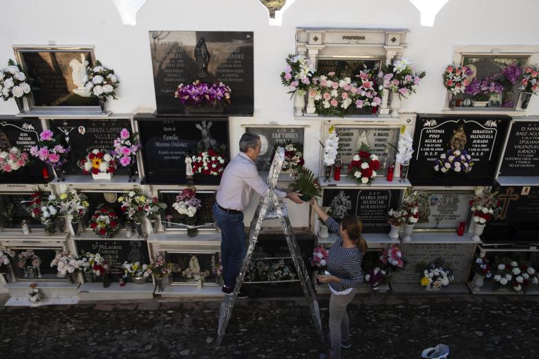 Unas personas colocan flores en un nicho en el cementerio de Casabermeja (Málaga)