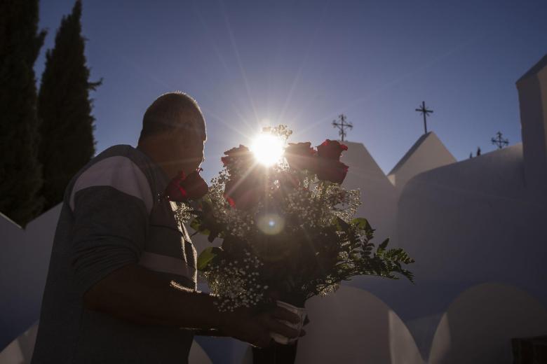Un hombre porta un centro de rosas en el cementerio de Casabermeja