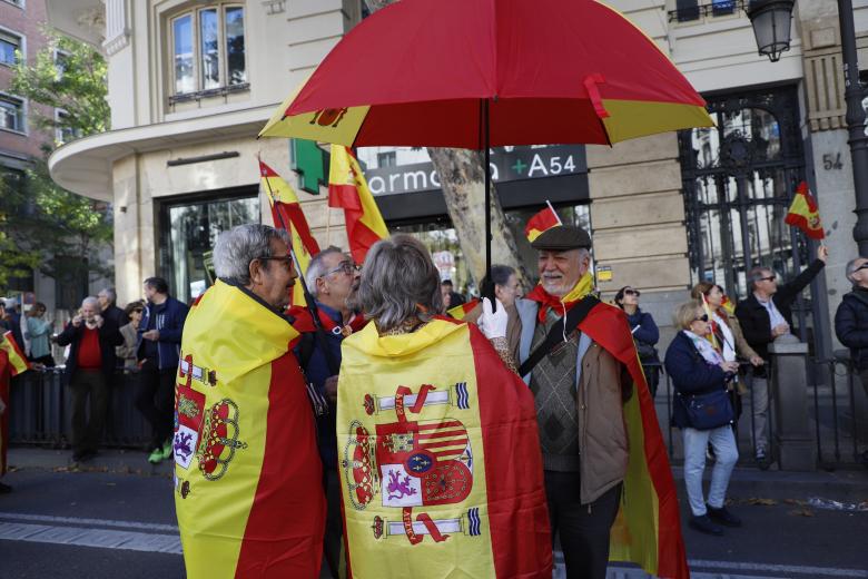 Asistentes se protegen del sol con banderas y paraguas de España.