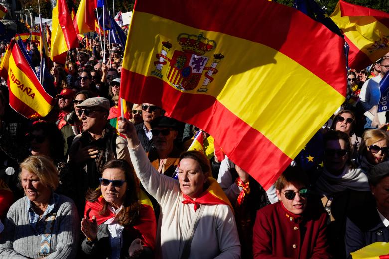 Una señora ondea una gran bandera de España rodeada de decenas de personas que no han dejado de gritar contra Sánchez.