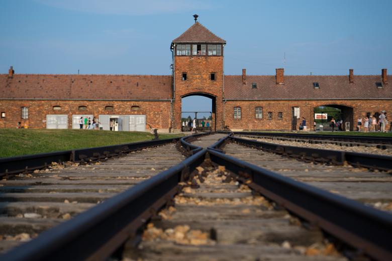 09 August 2018, Poland, Oswiecim: Visitors walk through the former extermination camp Auschwitz-Birkenau in front of the historic gate (inside). From 1940 to 1945, the SS operated the Auschwitz complex with numerous subcamps as extermination and concentration camps.