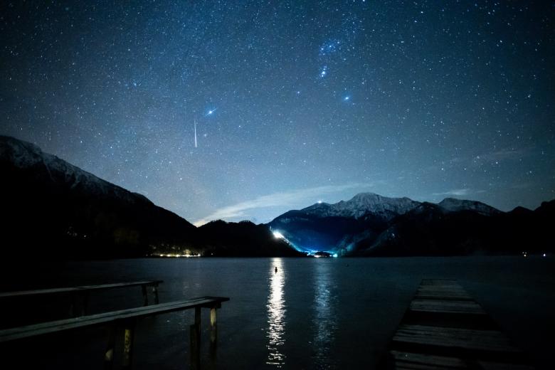 14 December 2020, Bavaria, Kochel Am See: A shooting star can be seen during the Geminiden meteor stream in the starry sky above the Kochelsee between the peaks of the Jochberg (l) and the Herzogstand. The Geminiden are the strongest meteor stream of the year.  *** Local Caption *** .