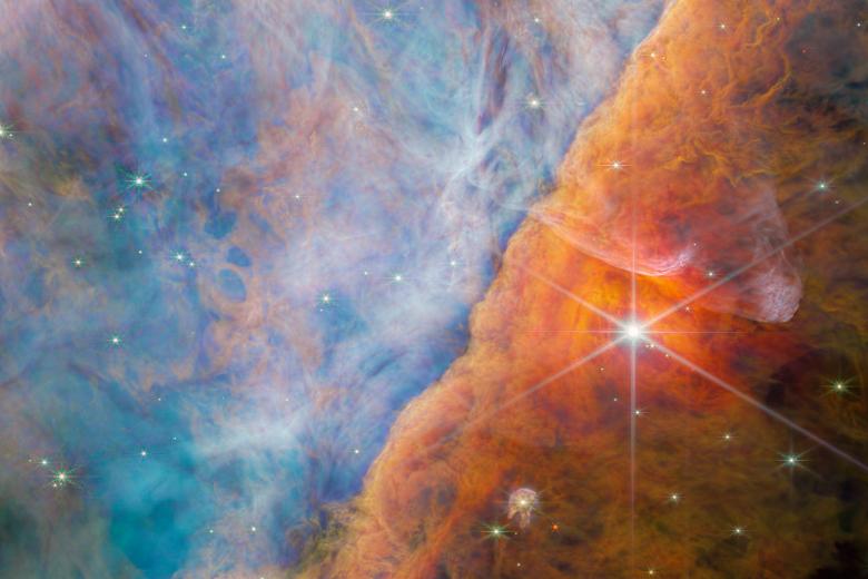 Nebulosa de Orión

Es ésta una región «donde la enérgica luz ultravioleta del cúmulo del Trapecio, ubicado en la esquina superior izquierda, interactúa con densas nubes moleculares. La energía de la radiación estelar está erosionando lentamente la Nebulosa de Orión, y esto tiene un profundo efecto en las moléculas y la química de los discos protoplanetarios que se han formado aquí alrededor de estrellas recién nacidas».

«Dentro de esta imagen se encuentra un sistema estelar joven conocido como d203-506, que tiene un disco protoplanetario. Los astrónomos utilizaron Webb para detectar por primera vez una molécula de carbono conocida como catión metilo en ese disco. Esa molécula es importante porque ayuda a la formación de moléculas más complejas a base de carbono».