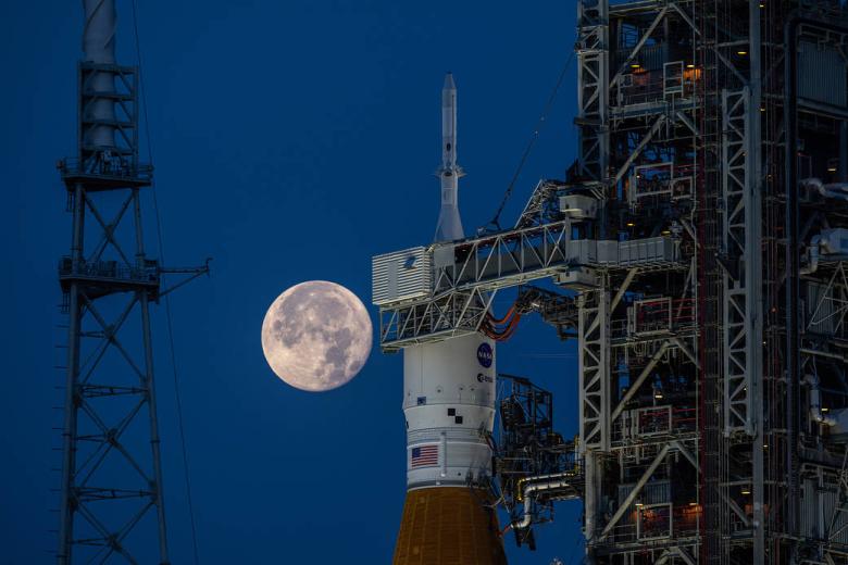 Una luna llena detrás del cohete Artemis I SLS (Sistema de lanzamiento espacial) y la nave espacial Orion en el Complejo de Lanzamiento 39B en el Centro Espacial Kennedy de la NASA