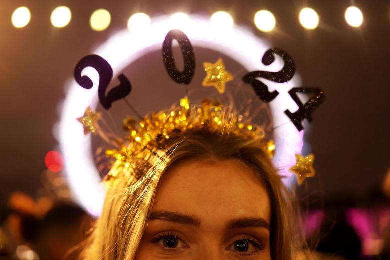 Una mujer celebra la entrada del Año Nuevo con una diadema del 2024 en la rivera del río Támesis en Londres, Reino Unido