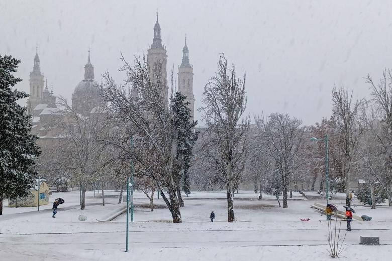 Varias personas caminan durante la nevada caída hoy viernes en Zaragoza, cerca de la Basílica del Pilar.