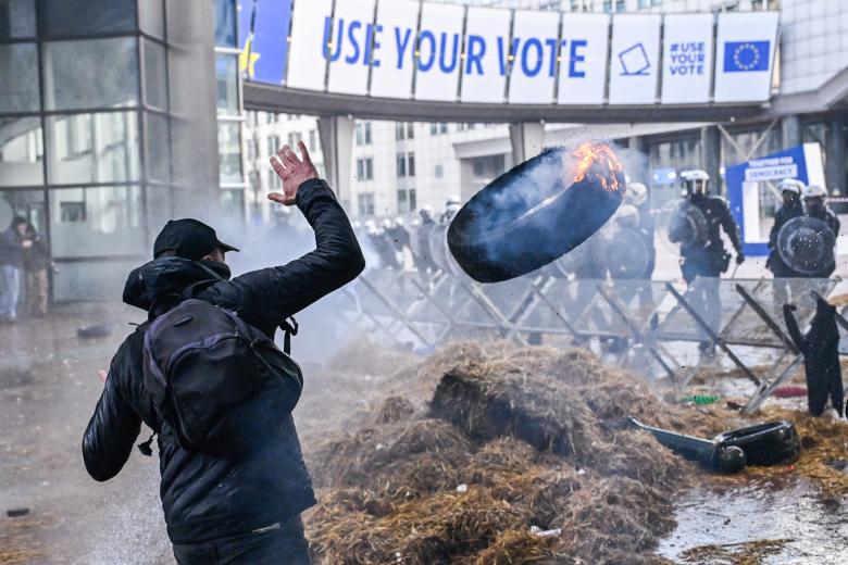 Un manifestante arroja un neumático ardiendo frente a las fuerzas policiales durante la acción de protesta de agricultores en el distrito europeo de Bruselas