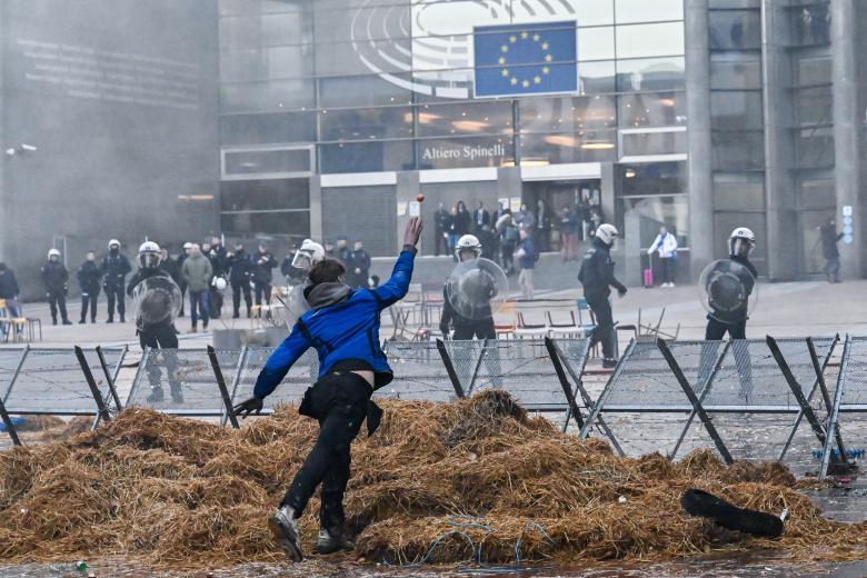 Un manifestante lanza un huevo a agentes de policía belgas cerca de la entrada del edificio del Parlamento Europeo durante la acción de protesta de los agricultores en el distrito europeo de Bruselas