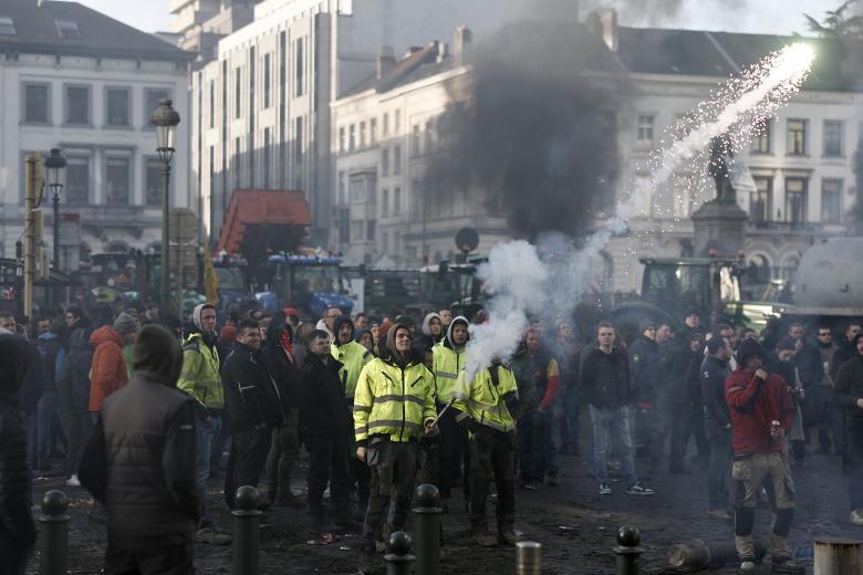Un manifestante lanza una bengala contra el edificio del Parlamento Europeo en Bruselascomo parte de la jornada de protestas en la que bloquearon las calles de la capital belga con 1.300 tractores mientras los líderes de la UE se reunían para una cumbre
