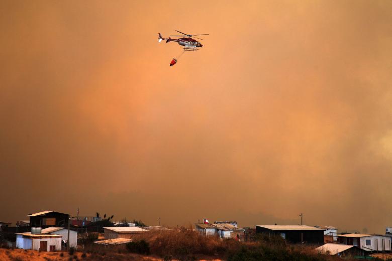 A helicopter works on the zone of a forest fire in the hills in Quilpe comune, Valparaiso region, Chile on February 3, 2024. The region of Valparaoso and Viña del Mar, in central Chile, woke up on Saturday with a partial curfew to allow the movement of evacuees and the transfer of emergency equipment in the midst of a series of unprecedented fires, authorities reported. (Photo by Javier TORRES / AFP)