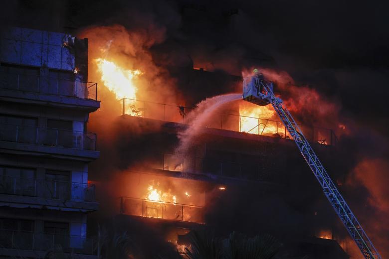 Bomberos trabajan en el incendio declarado sobre las cinco y media de esta tarde en un quinto piso de un edificio de viviendas de València que ha afectado totalmente al inmueble y se ha propagado a otro anexo, y los bomberos intentan aún rescatar a vecinos desde los balcones