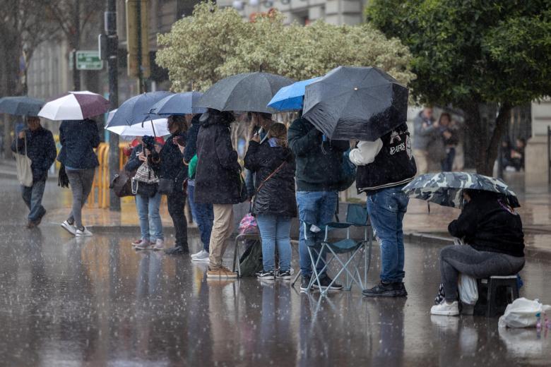 Varias personas se protegen de la lluvia con paraguas mientras guardan sitio, a primera hora de la mañana de este sábado, para contemplar el disparo de la mascletá frente al Ayuntamiento de Valencia